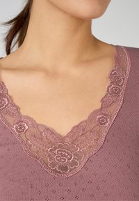 Short-sleeved, mauve top featuring floral lace trim at the V-neck and textured knit fabric with small dot patterns.