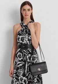 Abito nero a fiori con collo a halter, decorato con motivi floreali bianchi, cinte da una cintura nera; abbinato a una piccola borsa nera con hardware dorato.