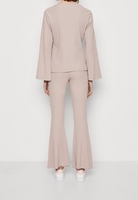 Beige žebrovaný top s dlouhým rukávem a odpovídající kalhoty se zvonovým střihem. Obsahuje jemnou texturu a uvolněný střih. Nosit s bílými teniskami.