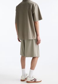 Kortærmet, kravebeklædt skjorte i olivengrøn, parret med matchende knælange shorts. Båret med hvide sneakers med bordeauxfarvede detaljer.