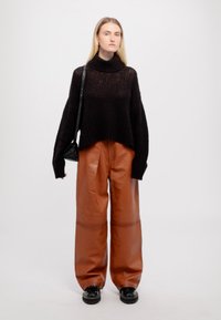 Schwarzer, grob gestrickter Rollkragenpullover, braune Leder-Hosen mit weitem Bein, schwarze Umhängetasche und klobige schwarze Schuhe. Einfaches und modernes Design.