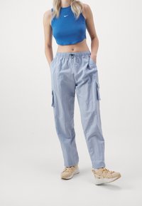 Světlé modré cargo kalhoty s elastickým pasem a bočními kapsami, doplněné o přiléhavý modrý top bez rukávů a béžové tenisky.