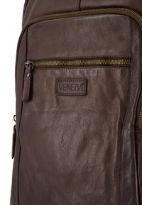 Bruine leren rugzak met een opvallende voorzak met ritssluiting, gouden hardware en een klein leren logo-opdruk. Textuur van het oppervlak.