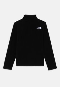 Svart fleece-pullov med hög krage och långa ärmar. Har en vit logotyp på övre vänstra sidan. Mjuk textur, minimalistisk design.