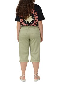 Lichtgroene cropped broeken met opgerolde boorden, gecombineerd met een zwart T-shirt met een gele zonafbeelding en bold rode letters op de achterkant.