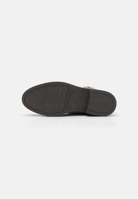 Suola di una scarpa con forma arrotondata, materiale in gomma nera, motivo testurizzato e tre scanalature orizzontali vicino al tallone per una migliore aderenza.