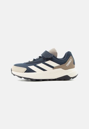Børnesneaker i navy og beige med hvide striber, velcrolukning, polstret sål og "TERREX" mærke ved hælen.
