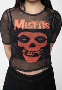 Black mesh cropped t-shirt featuring red skull graphic and "Misfits" text. Short sleeves with a fitted design and subtle skull patterns.
