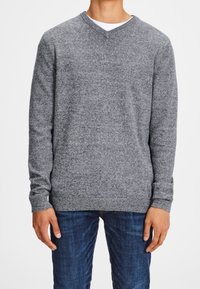 Grauer V-Ausschnitt-Pullover aus weichem Material, mit geripptem Saum und Ärmeln, kombiniert mit dunkelblauen Jeans. Minimalistisches Design und Textur.