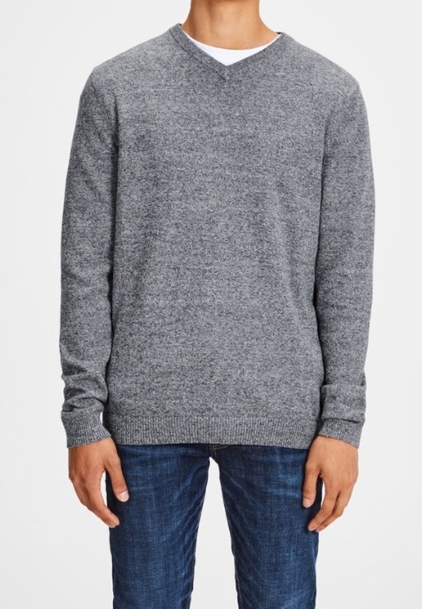 Grauer V-Ausschnitt-Pullover aus weichem Material, mit geripptem Saum und Ärmeln, kombiniert mit dunkelblauen Jeans. Minimalistisches Design und Textur.