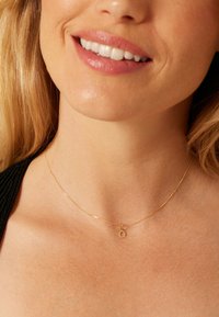 Gold necklace with a delicate chain featuring a small, circular charm engraved with the letter "Q." Smooth texture and minimal design.