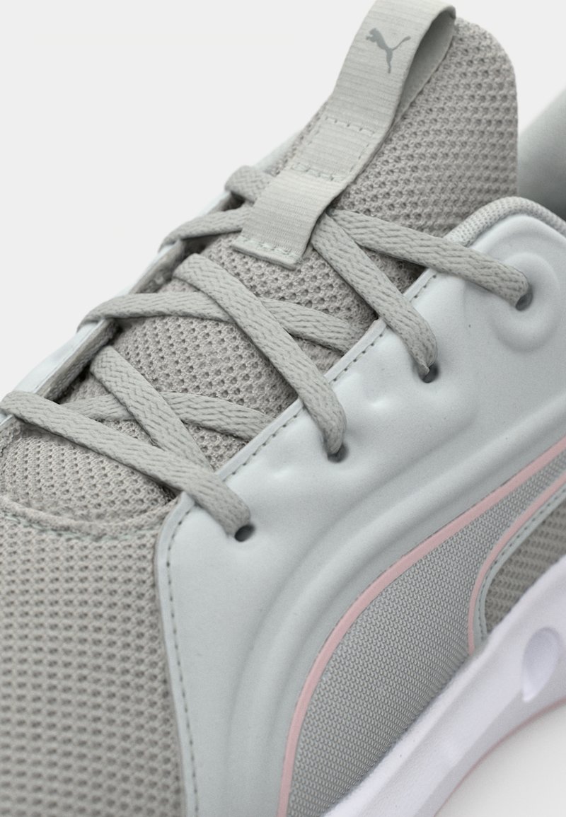 Zapatilla deportiva gris con parte superior de malla y acentos texturizados. Los detalles incluyen rayas rosa claro y una suela de goma flexible.