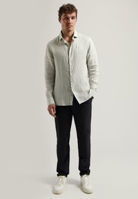 Lichtgroen linnen overhemd met knopen en een relaxte pasvorm, gecombineerd met donkere broek en witte sneakers, met lange mouwen en een zachte textuur.