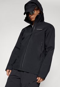 Veste imperméable noire avec un col haut, fermeture éclair à l'avant, poches latérales et capuche. Texture lisse avec une finition mate et un branding minimal.