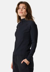 Svart zip-up jacka med hög krage, ribbad textur och långa ärmar. Den har sidofickor och synliga sömnadsdetaljer.