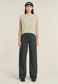 Top beige senza maniche con scollatura rotonda, abbinato a pantaloni cargo grigio scuro con molteplici tasche e vita con cordino.