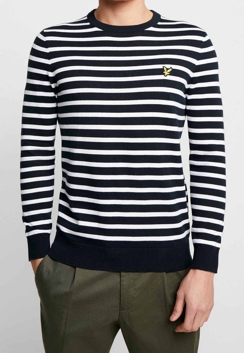 Navy ja valge triibuline sviiter, millel on ümar kaelus, soonikkoes varrukad ja alumine äär, ning rinnal on väike kollane logo.