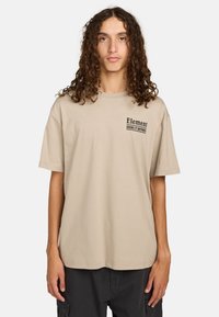 Beige oversized t-shirt with short sleeves, featuring "Element" logo and text printed in black on the left chest area. Smooth cotton texture.