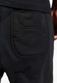 Black sweatpants featuring a distinct back pocket with rounded edges, made of soft, textured fabric, highlighting a sturdy stitching detail.