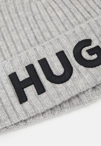 Berretto grigio lavorato a maglia con texture a coste, che presenta un grande ricamo nero "HUG" sul risvolto.