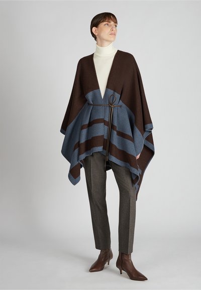 Bruine en blauwe gestreepte poncho met een diepe V-hals, gecombineerd met grijze gestructureerde broeken en bruine laarzen met hak, cinched bij de taille.