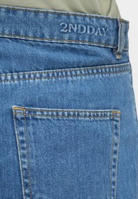 Jeans hlače iz jeansa svetlo modre barve z vidnimi poudarki šivov, zadnjim žepom in značilno etiketo "2NDDAY" na pasu.