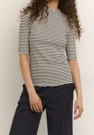 Sort-hvid stribet ribstrikket top med en bølget halsudskæring og korte ærmer, båret med mørke bukser med nålestriber.