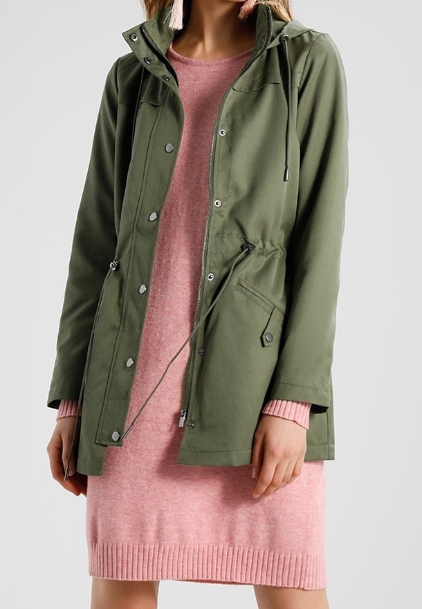 Veste utilitaire vert olive avec taille ajustable par cordon, fermetures par boutons-pression et capuche, portée sur une robe en maille rose avec ourlet côtelé.
