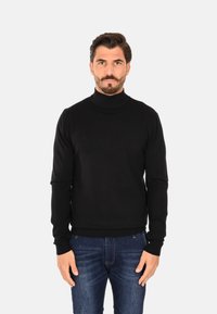 Maglione a collo alto nero realizzato in materiale morbido, con maniche lunghe e polsini a costine, abbinato a jeans denim blu.