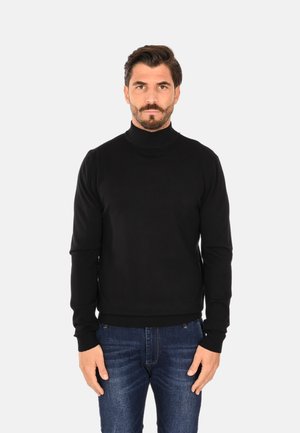 Maglione a collo alto nero realizzato in materiale morbido, con maniche lunghe e polsini a costine, abbinato a jeans denim blu.