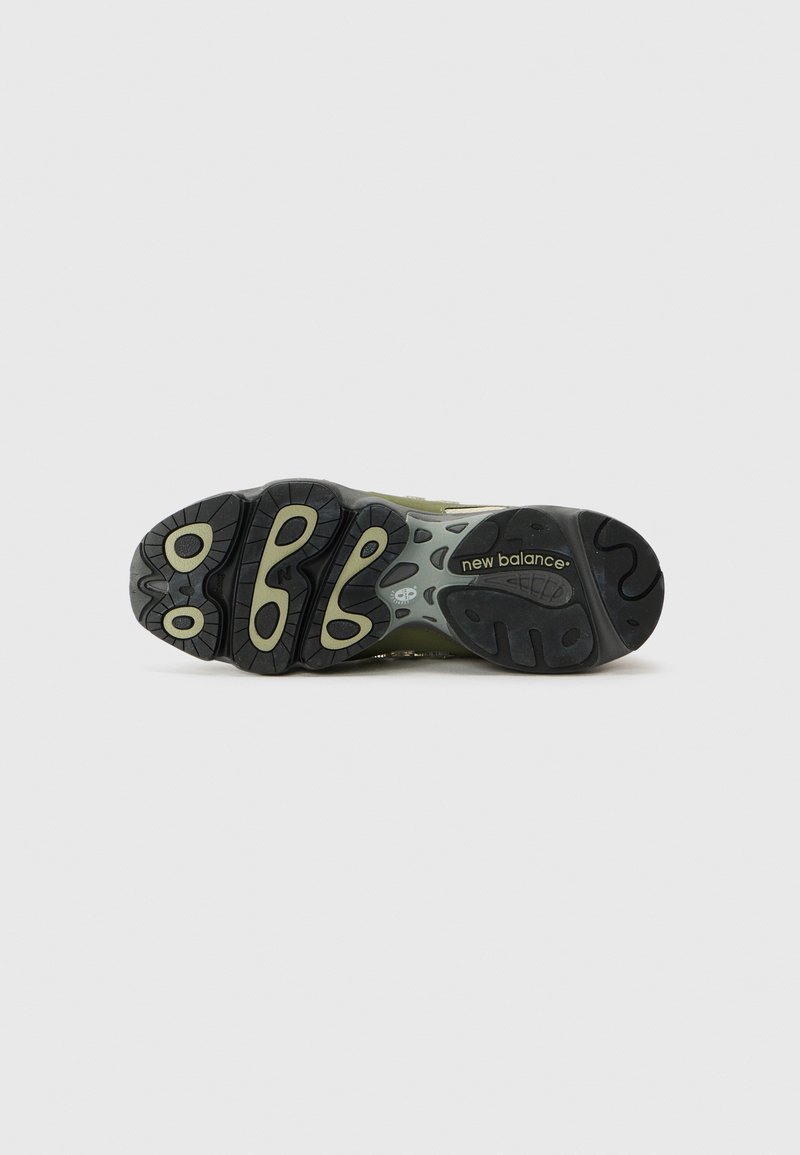 Suela de zapatilla deportiva en negro y verde con banda de rodadura estampada, que presenta un agarre texturizado y el logotipo de "New Balance" en dorado.