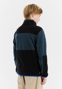 Fleecejack in zwart en teal. Kenmerken zijn een hoge kraag, een kleurblokkering ontwerp, lange mouwen en een blauwe rand aan de onderkant. Lichtgewicht, comfortabel materiaal.