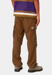 Pantalones cargo marrones con un corte holgado, que cuentan con bolsillos laterales y un parche con el logo. El material parece resistente con un acabado texturizado.