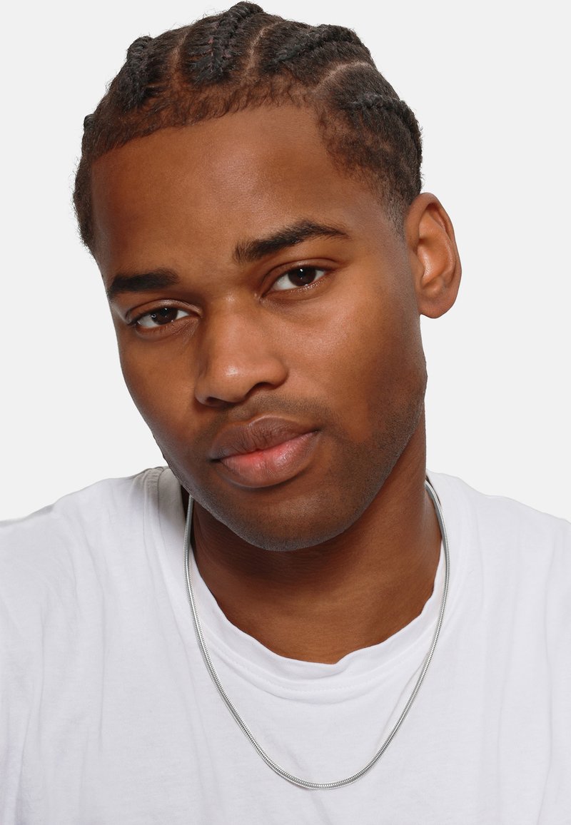 Collana di catena d'argento indossata sopra una maglietta bianca, con un primo piano di una persona con capelli intrecciati e un incarnato liscio.