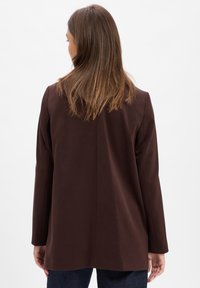 Braune, strukturierte Jacke mit langen Ärmeln, glatter Textur und minimalen Nähdetails. Verfügt über einen geraden Saum hinten und ein tailliertes Design.