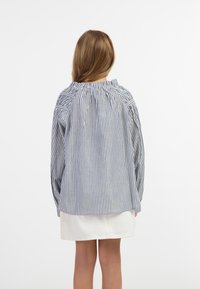 Stribet bomuldsbluse med en samlet halsudskæring og lange ærmer, med blå og hvide lodrette striber; båret over en hvid nederdel.