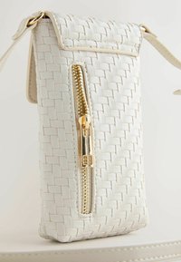 Kis fehér, szőtt bőrből készült keresztpántos táska arany cipzáras zsebbel elöl és állítható vállpánttal.