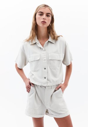 Lichtgrijs overhemd met korte mouwen, voorzien van twee voorzakken en knoopsluiting, gecombineerd met bijpassende ruime shorts. Zachte katoenstof.