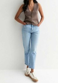 Brun ärmlös knäpp-top, ljusblå raka jeans och vita sneakers med bruna detaljer. Passformen är avslappnad och ledig.