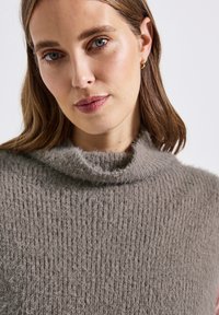 Pull en tricot gris avec une texture douce et duveteuse et un col roulé haut. Larges côtes verticales visibles sur tout le tissu.