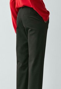 Schwarze, maßgeschneiderte Hose mit glatter Textur, geradem Schnitt und dezenten Gesäßtaschen. Kombiniert mit einem roten Pullover für einen Kontrast.