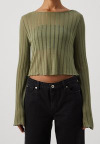 Grünes, geripptes Langarmoberteil mit einem cropped Design, das über einen Rundhalsausschnitt und eine lockere Passform verfügt, kombiniert mit hochgeschnittenen schwarzen Jeans.