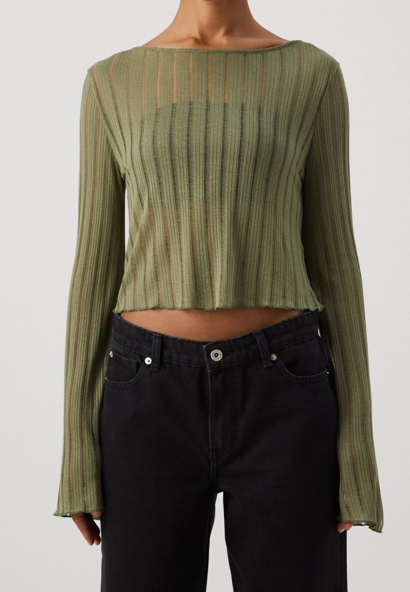 Grünes, geripptes Langarmoberteil mit einem cropped Design, das über einen Rundhalsausschnitt und eine lockere Passform verfügt, kombiniert mit hochgeschnittenen schwarzen Jeans.