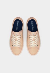 Ζευγάρι ανοιχτό ροζ αθλητικά παπούτσια Calvin Klein με λευκά κορδόνια, μπλε εσωτερικά πέλματα και λογότυπα της μάρκας στη γλώσσα και στην πλευρά, σε λευκό φόντο.