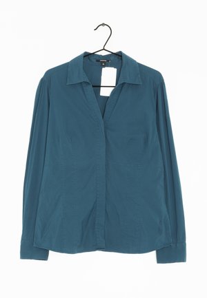 Camicia a maniche lunghe color turchese con colletto, chiusura frontale a bottoni e tasche laterali. Realizzata in tessuto morbido con una vestibilità leggermente rilassata.