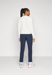 Witte gestructureerde lange mouwtop met navy slim-fit broek en lichtgrijze sneakers met roze accenten, gezien vanuit de achterkant.