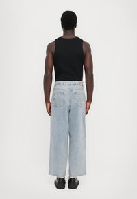 Top slim preto sem mangas com jeans de perna larga azul claro, apresentando um rótulo de cintura em contraste e bolsos traseiros. Sapatos pretos.
