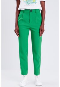 Green tailored pants with a smooth texture, featuring a single front pleat and a button closure at the waist, paired with white sneakers.