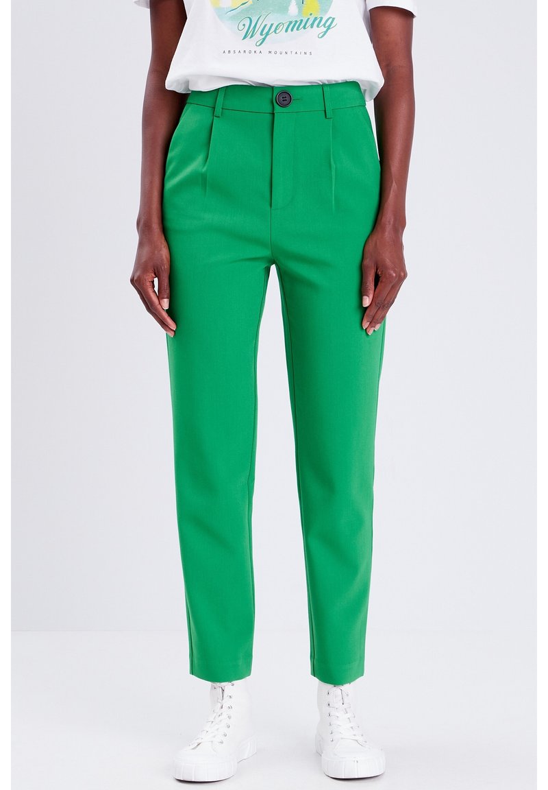 Green tailored pants with a smooth texture, featuring a single front pleat and a button closure at the waist, paired with white sneakers.
