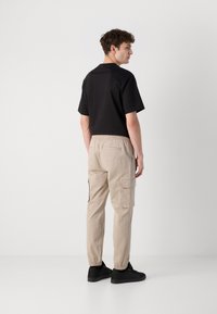 Zwarte korte mouwen t-shirt gecombineerd met beige cargobroek, met elastische manchetten en zijzakken, gedragen met zwarte schoenen.